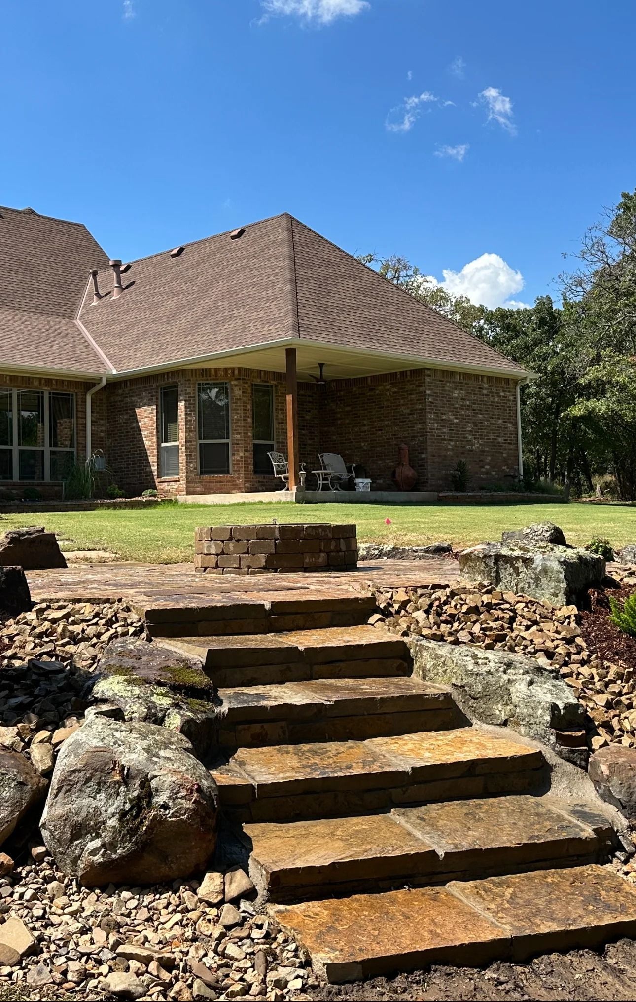 Stone steps lead to a brick house with a brown tiled roof and green lawn on a sunny day