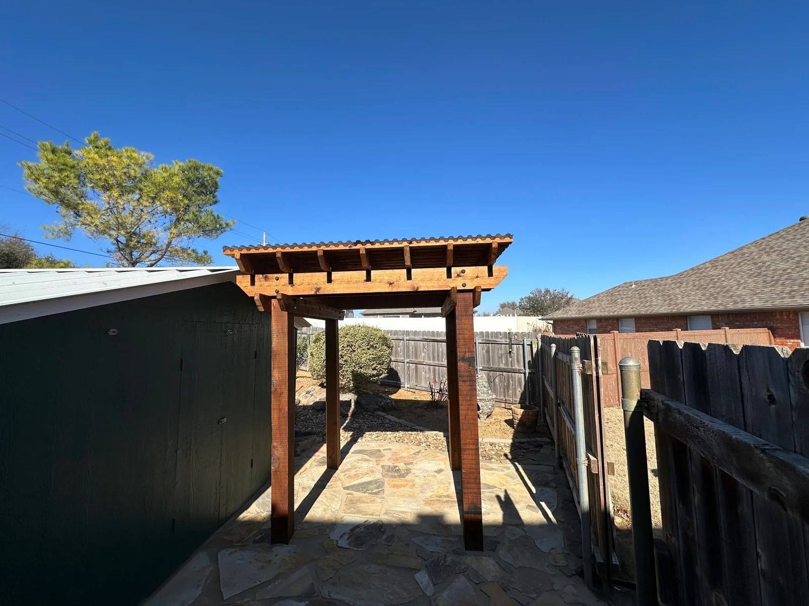Wooden pergola walkway between fences in a sunny backyard with blue sky