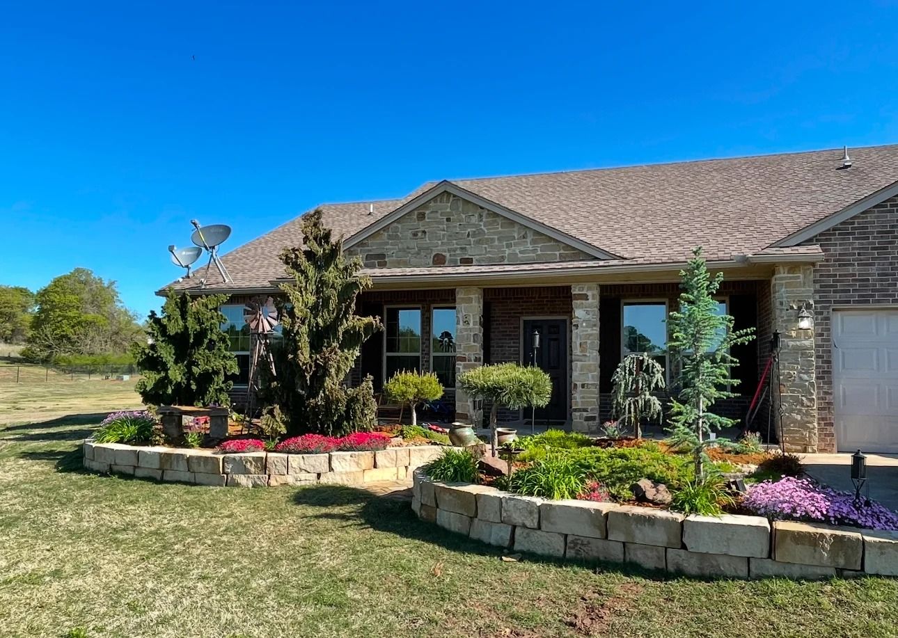 Single-story house with a landscaped front garden, stone borders, and a clear blue sky