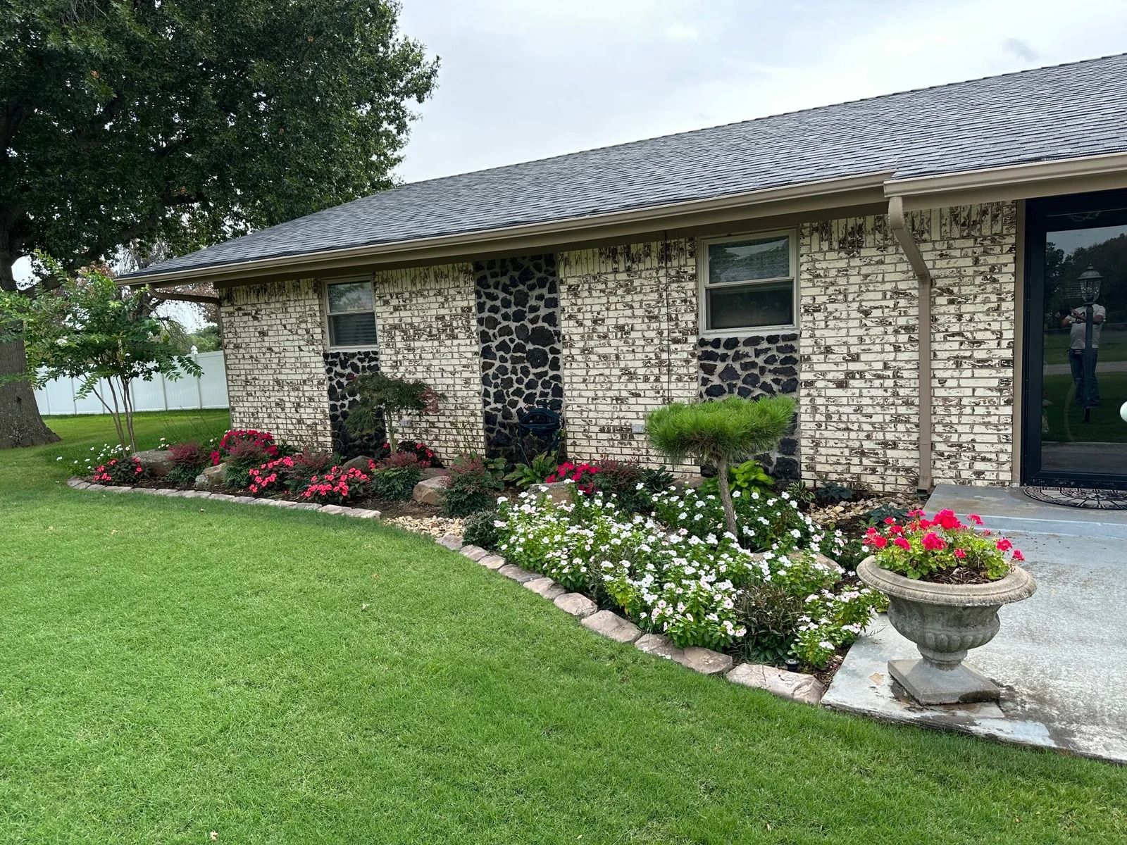 Brick house with manicured lawn, flower beds, and a potted planter by the front walkway