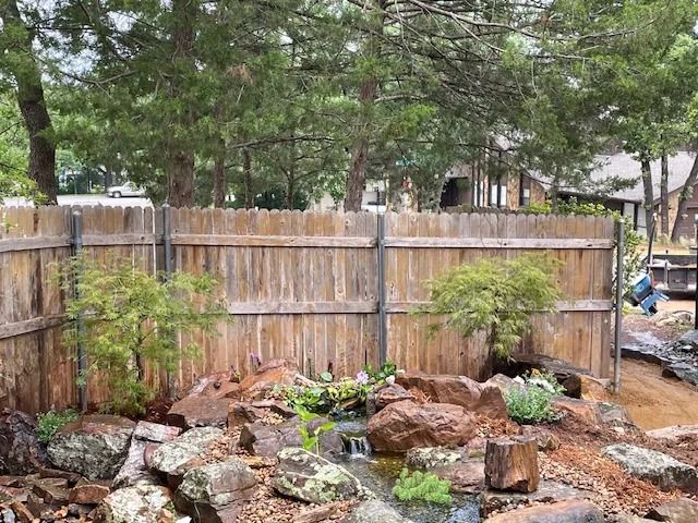 Backyard garden with wooden fence, rocks, shrubs, and tall trees after rain