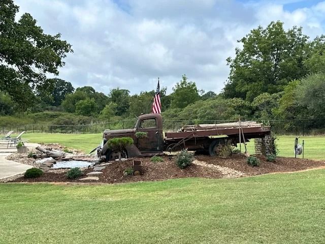 Old rusty truck sculpture with an American flag on a landscaped roadside display