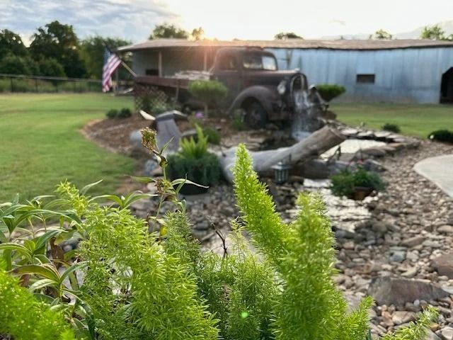 Garden waterfall and pond beside a rustic truck sculpture near a building at sunset