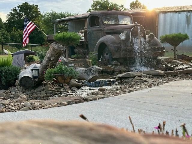 Old truck fountain in a rock garden with water cascading beside an American flag.