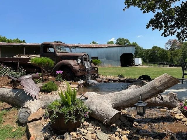 Old truck fountain beside a pond and rocks in a sunny landscaped garden