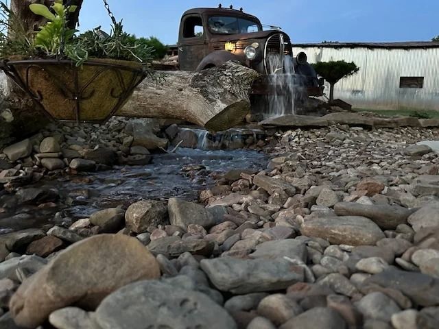Old rusty truck pouring water over rocks in a garden-like yard