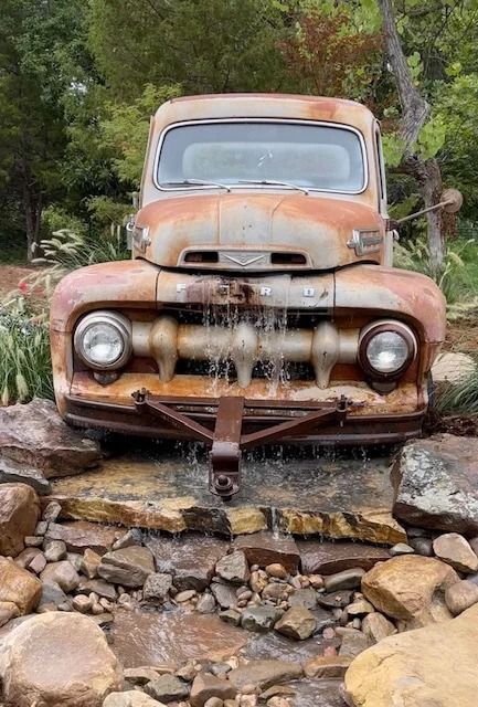 Rusty old pickup truck crossing a rocky stream, water pouring from the front grille.