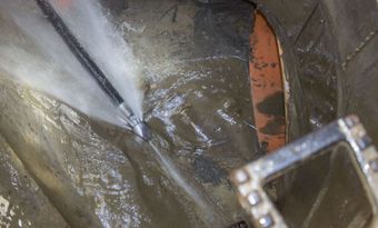 A person is using a high pressure hose to clean a drain.