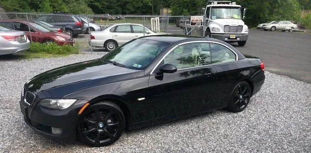 A black bmw 3 series convertible is parked in a gravel lot.