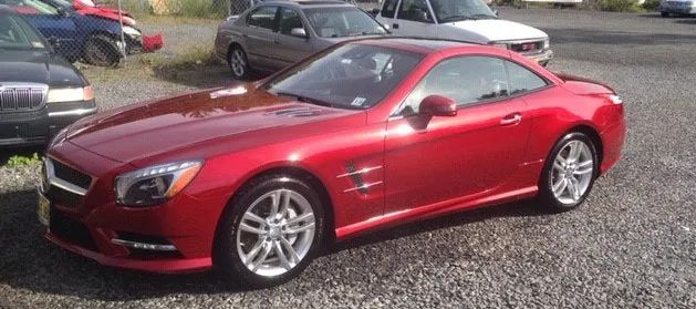 A red sports car is parked in a gravel lot.