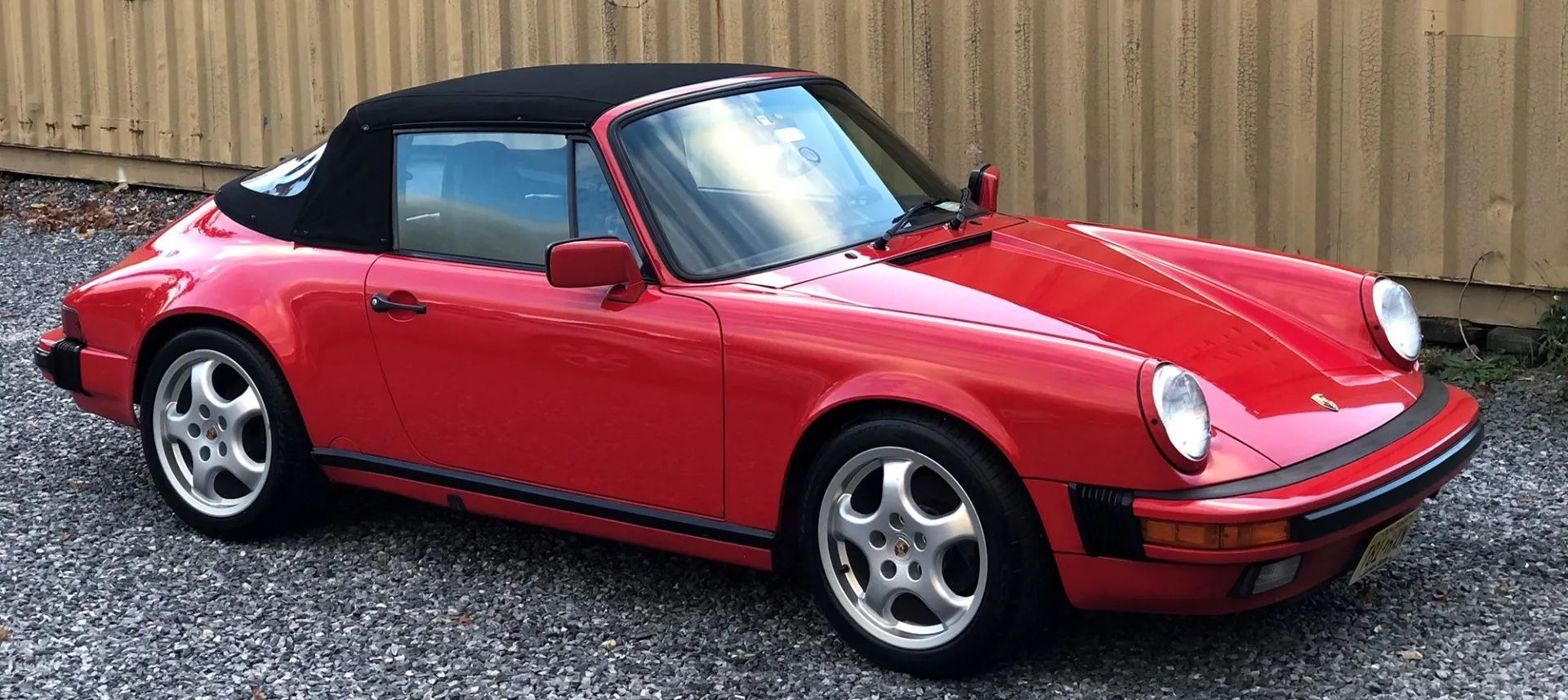 A red porsche 911 convertible with a black top is parked in a gravel lot.
