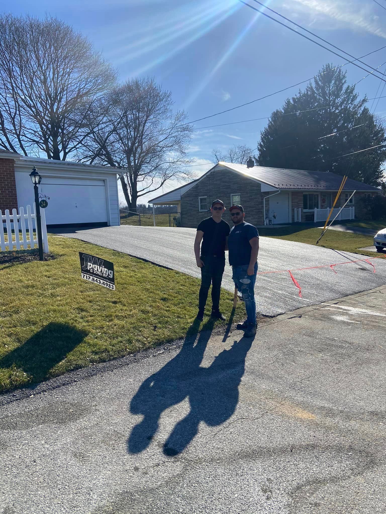 Two people stand on a newly paved gravel driveway in front of a residential house on a sunny day.