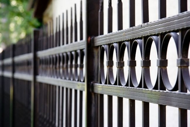 Black metal fence with decorative circle details, against a white wall, outdoors.