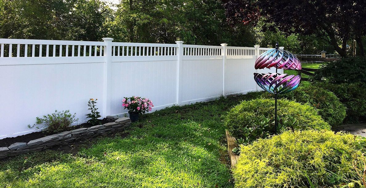 A white fence surrounds a lush green yard with a windmill in the background.