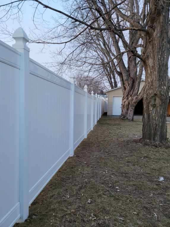 A white fence surrounds a yard with trees and a garage.