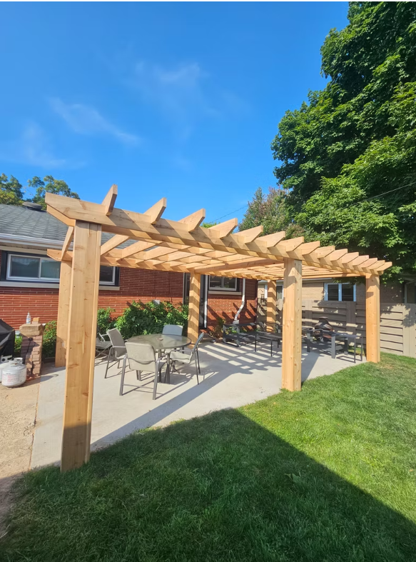 Wooden pergola over patio with table, chairs, and green grass under a blue sky.