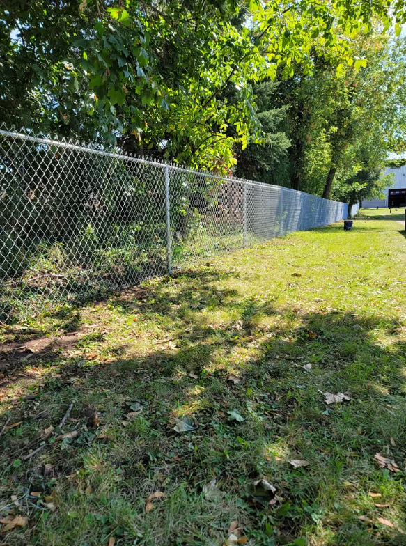 A chain link fence is surrounding a lush green field.