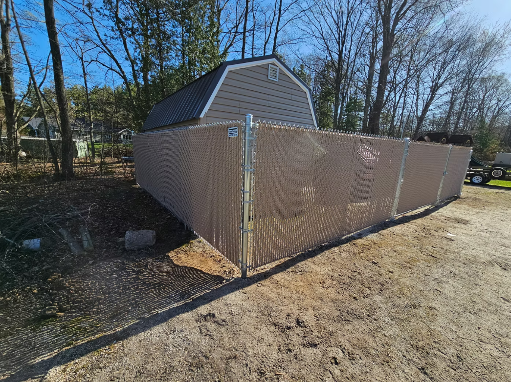 A shed is behind a chain link fence.
