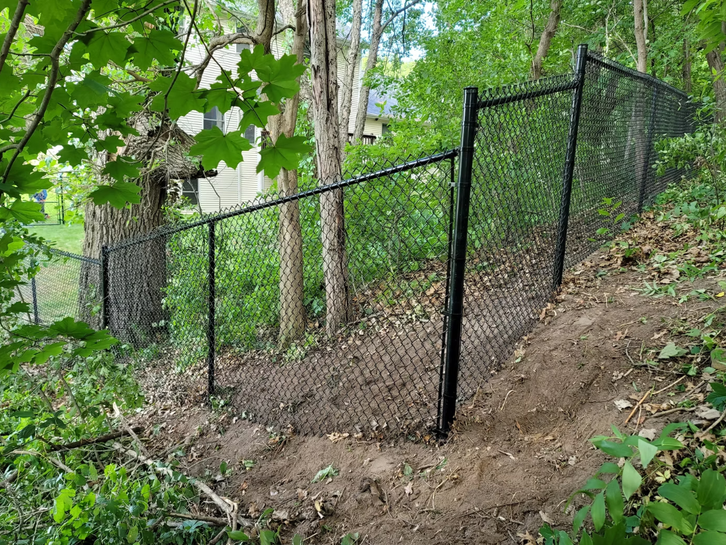 A chain link fence surrounds a dirt path in the woods.