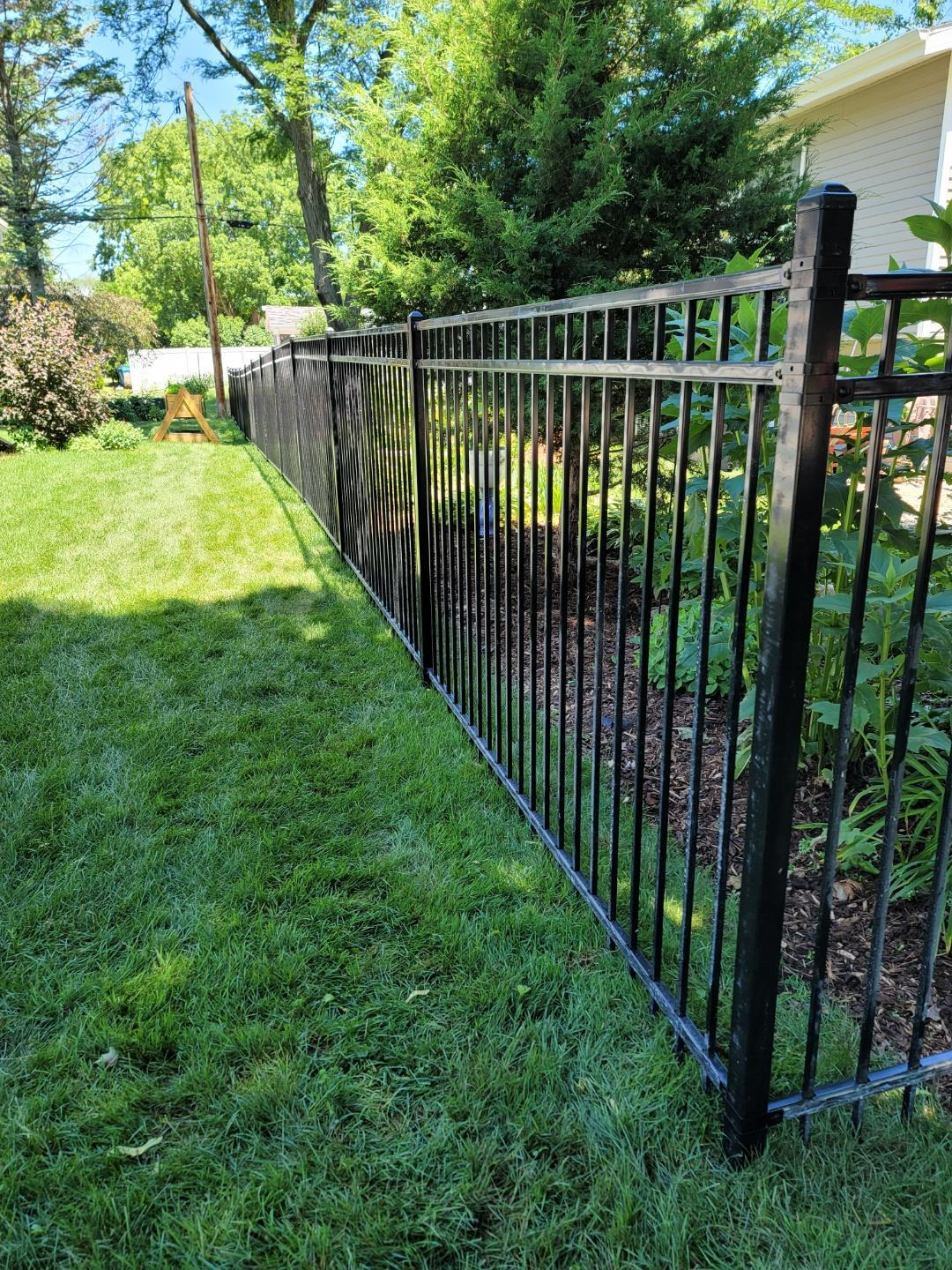 A black metal fence surrounds a lush green yard.