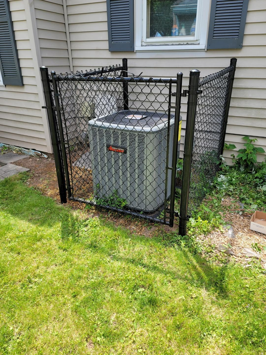 An air conditioner is behind a chain link fence in the backyard of a house.