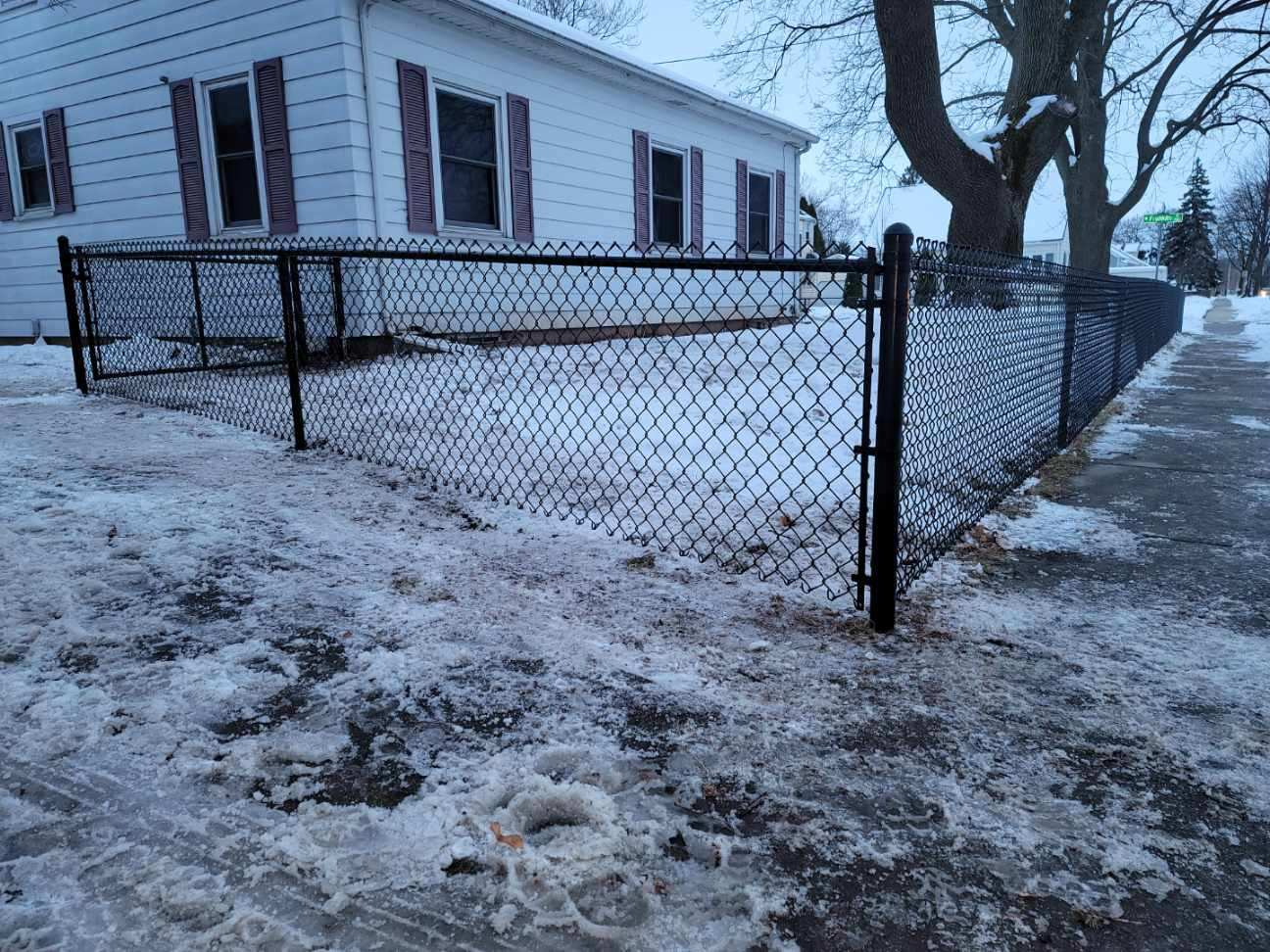 A chain link fence is surrounded by snow in front of a house.