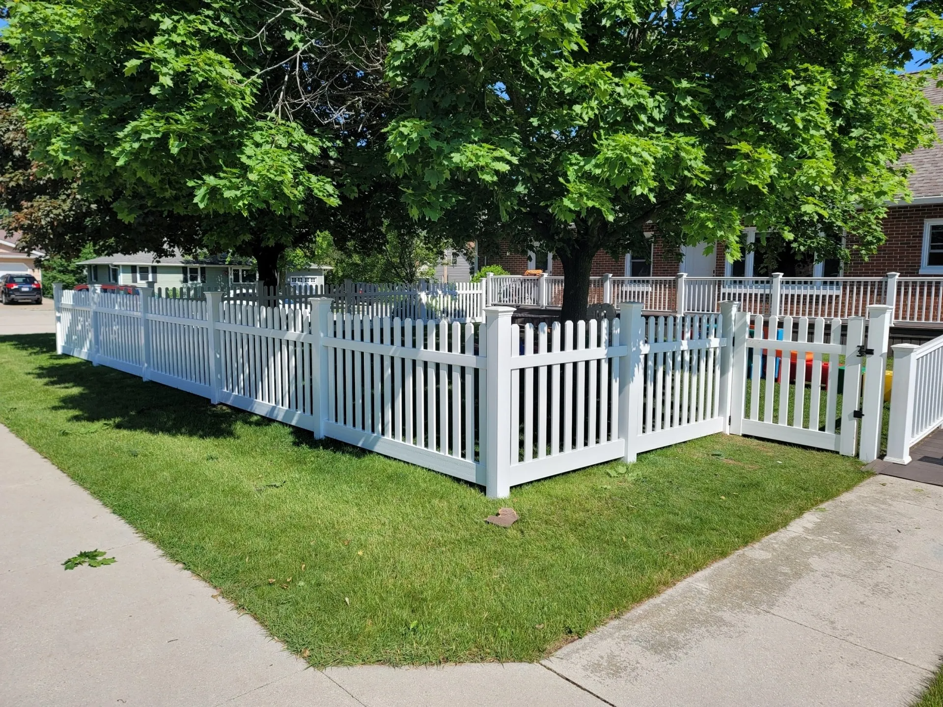 A white picket fence surrounds a lush green yard in front of a house.