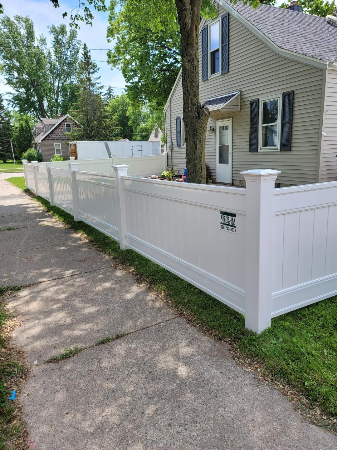 A white vinyl fence is sitting next to a house on a sidewalk.