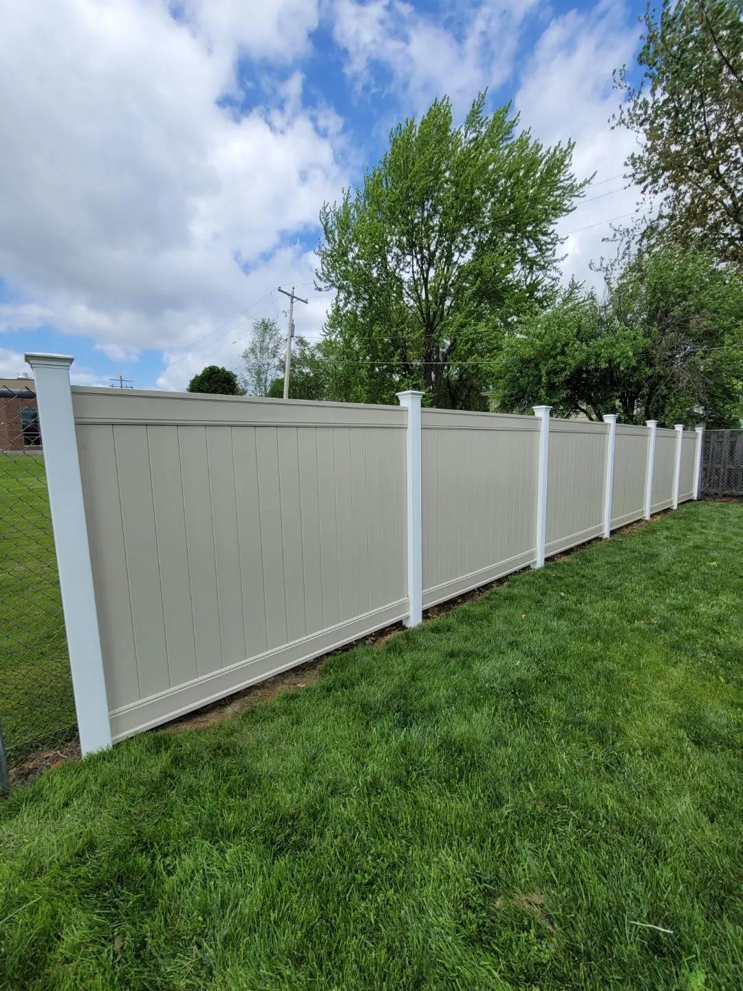 A white vinyl fence is sitting in the middle of a lush green field.