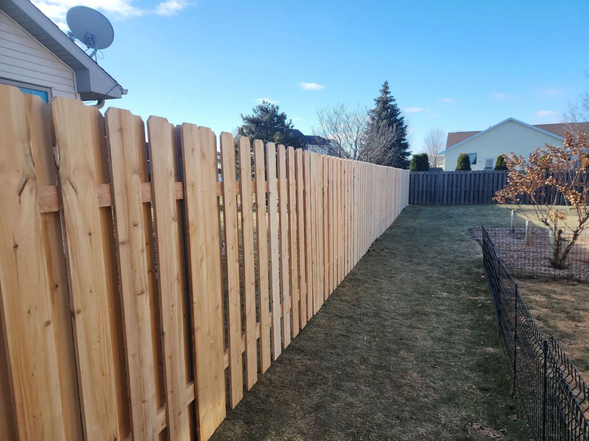 A newly built wooden fence runs along a grassy backyard under a clear blue sky.