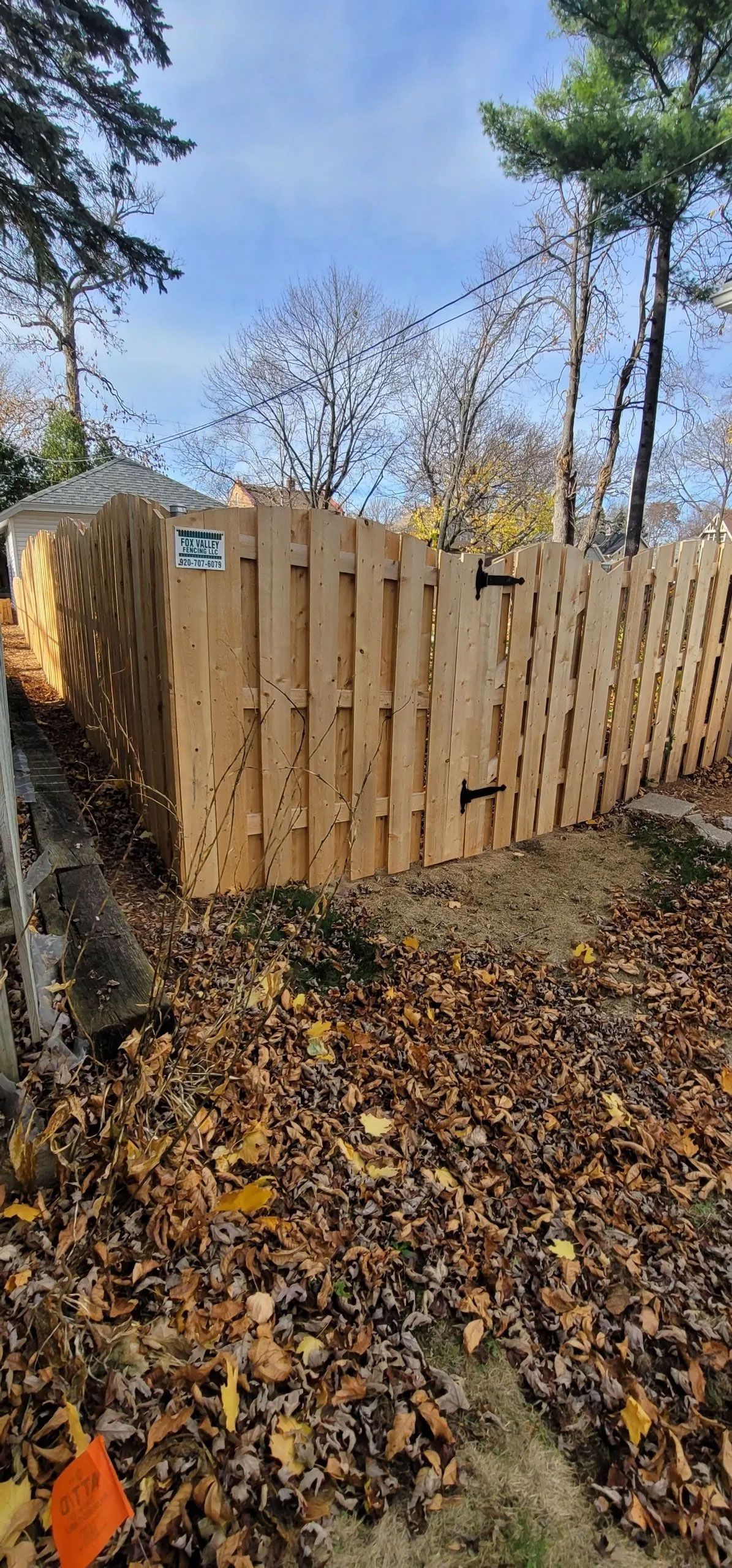 Wooden fence with a gate, number 35 on it, surrounded by fallen leaves. Trees and blue sky in the background.