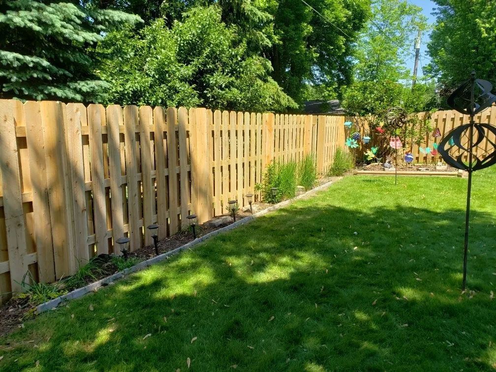 Wooden fence bordering a green lawn, trees in the background.