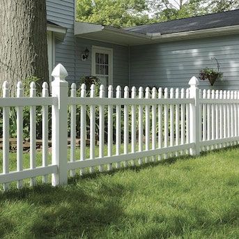 A white picket fence surrounds a lush green yard in front of a house.