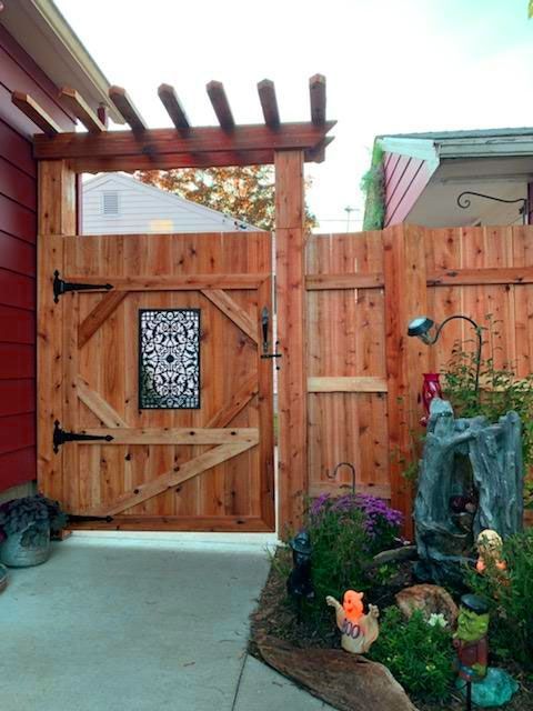 Wooden gate with a decorative iron panel and a pergola, leading into a garden.