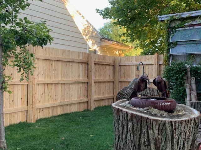 A wooden fence surrounds a stump in a backyard.