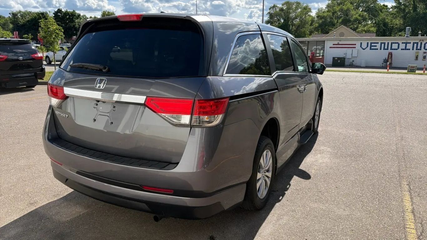 Gray minivan parked in a sunny parking lot, rear view with taillights visible