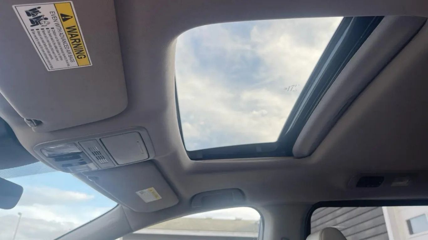Car interior with sunroof open to a cloudy sky, showing the headliner and windshield area.