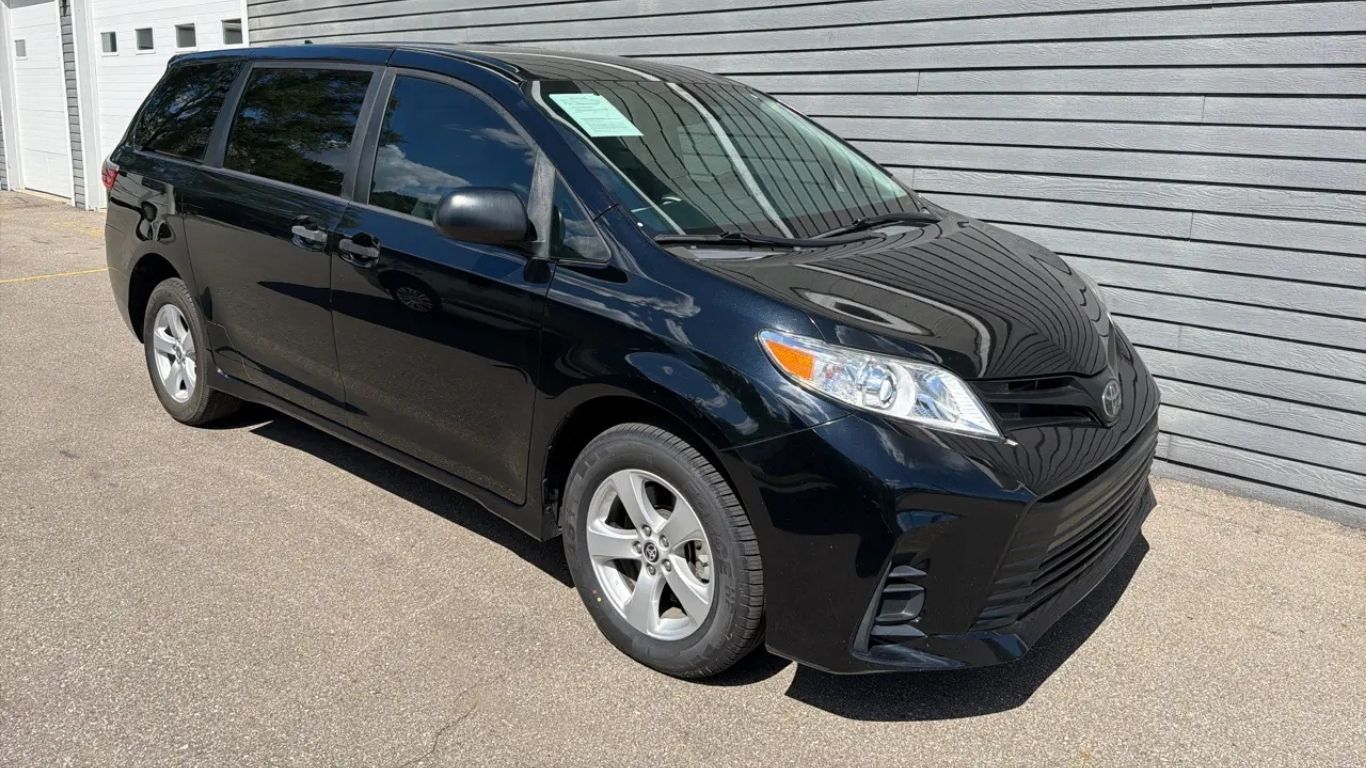 Black hatchback car parked beside a corrugated metal wall in daylight