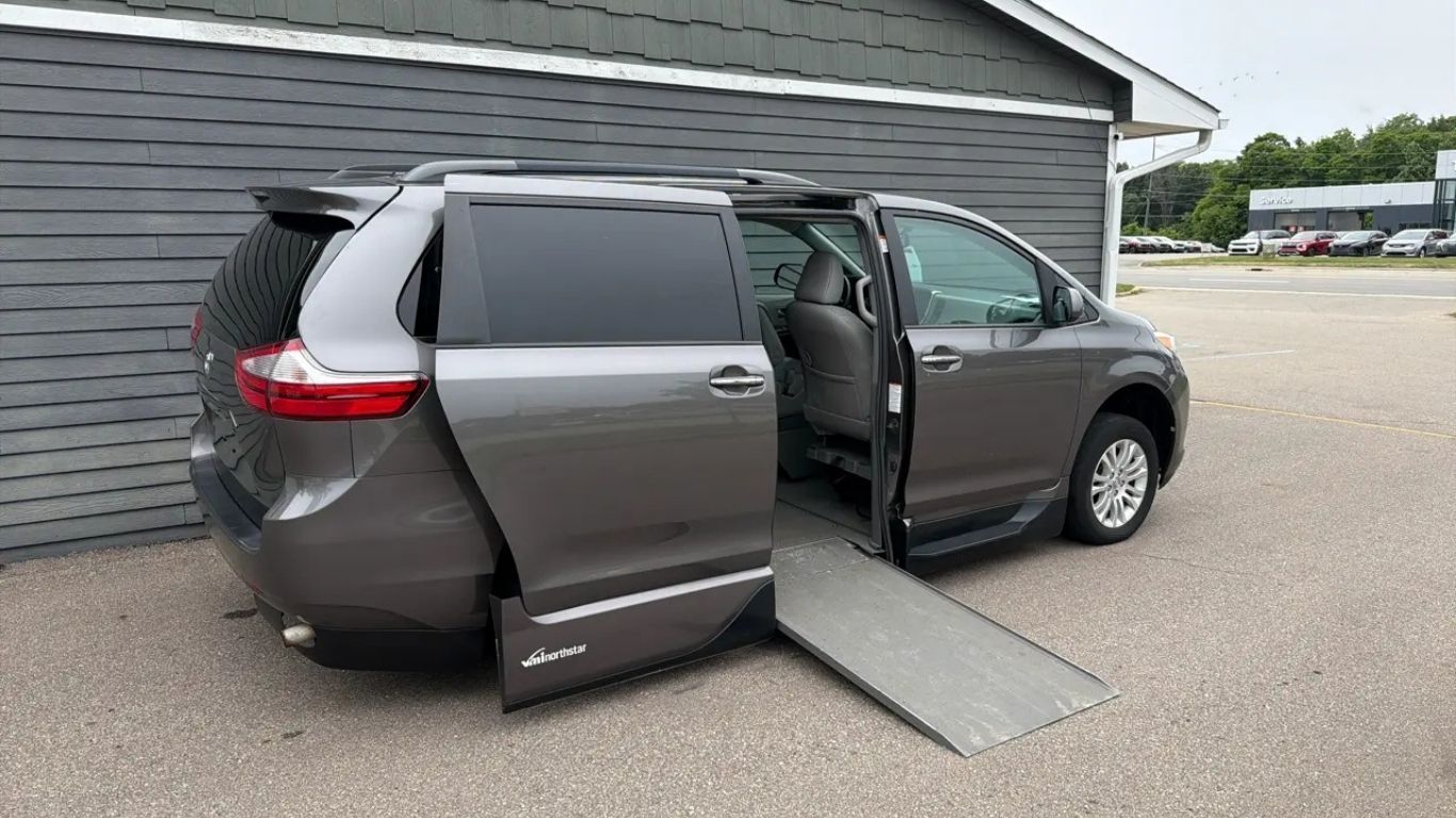 Gray minivan with wheelchair ramp deployed in a parking lot beside a building
