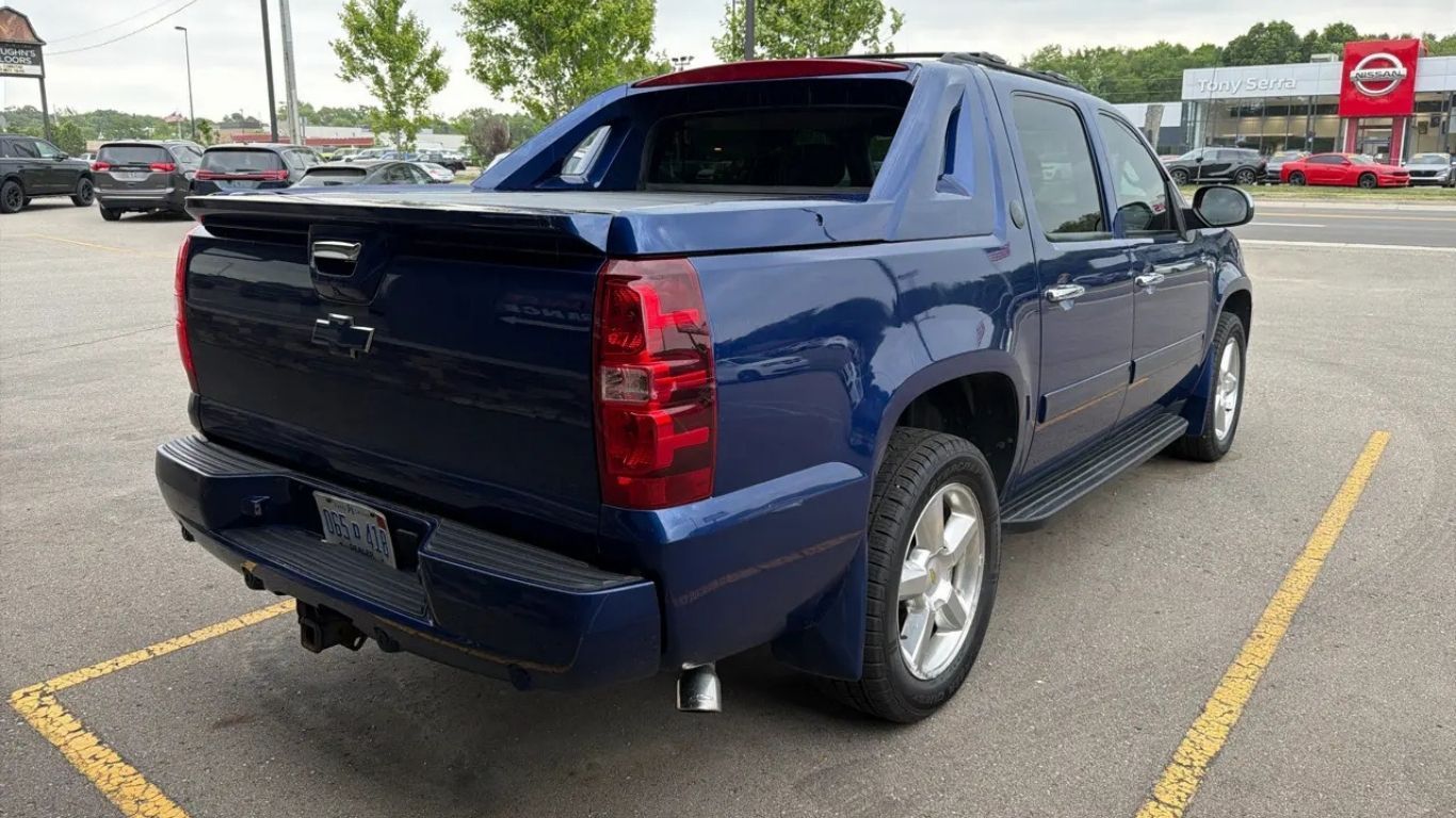 Dark blue pickup truck parked in a lot, rear three-quarter view, near yellow lines and a stop sign.