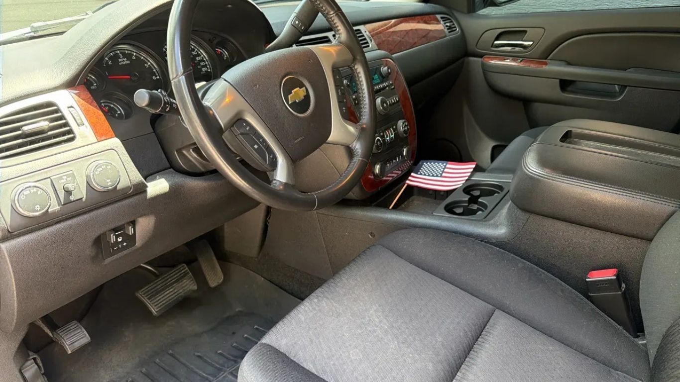 Car interior with black seats, steering wheel, dashboard, and wood trim, viewed from the driver’s side.