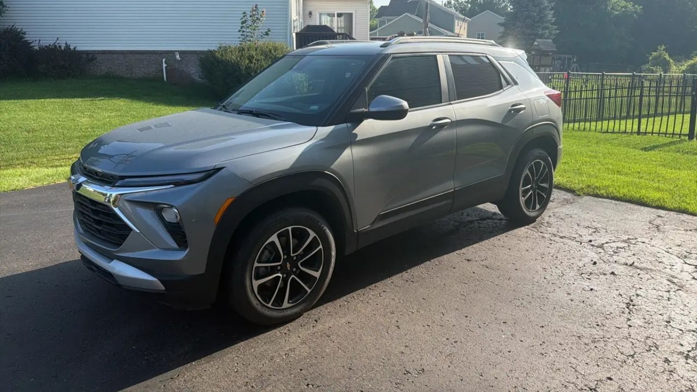 Gray SUV parked on a driveway in front of a house, with green lawn and bright sunlight.