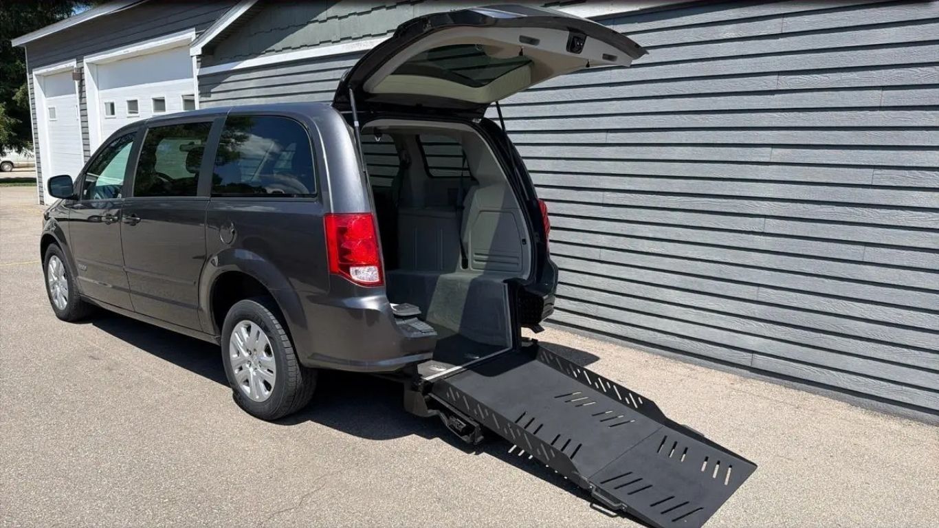 Gray minivan with rear hatch open and wheelchair ramp deployed beside a building