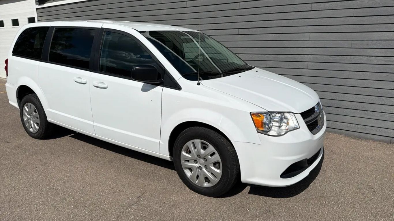 White minivan parked on pavement in front of a gray building wall