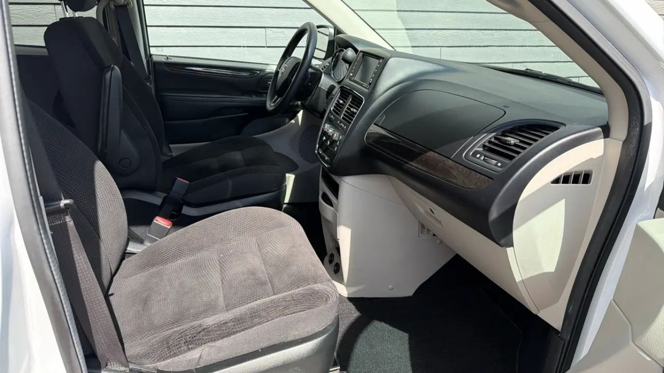 Car interior with front passenger door open, showing gray seats and dashboard.