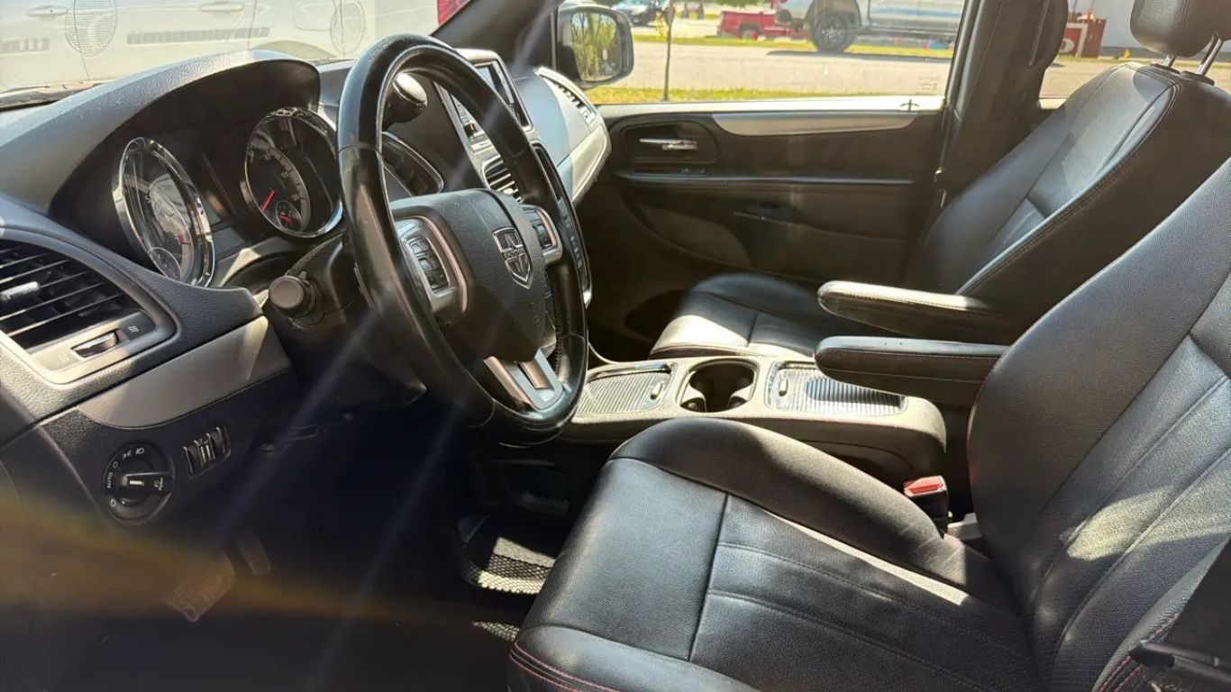 Car interior with black leather seats, steering wheel, and center console in sunlight