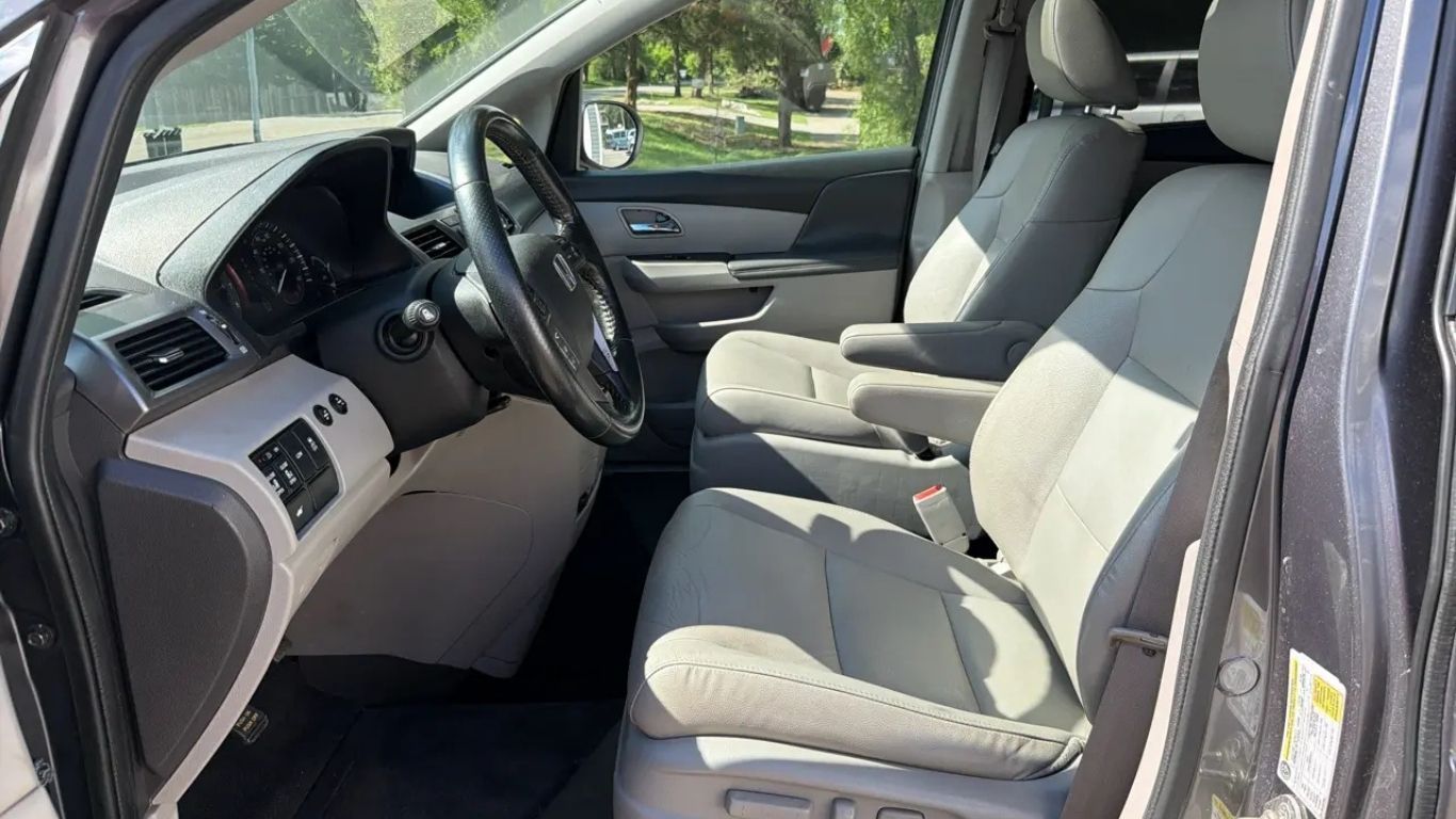 Open front car interior with beige seats, gray dashboard, and steering wheel visible from the driver’s side.