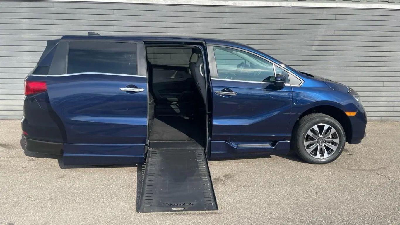 Blue minivan with a wheelchair ramp extended from the open side door in a parking lot