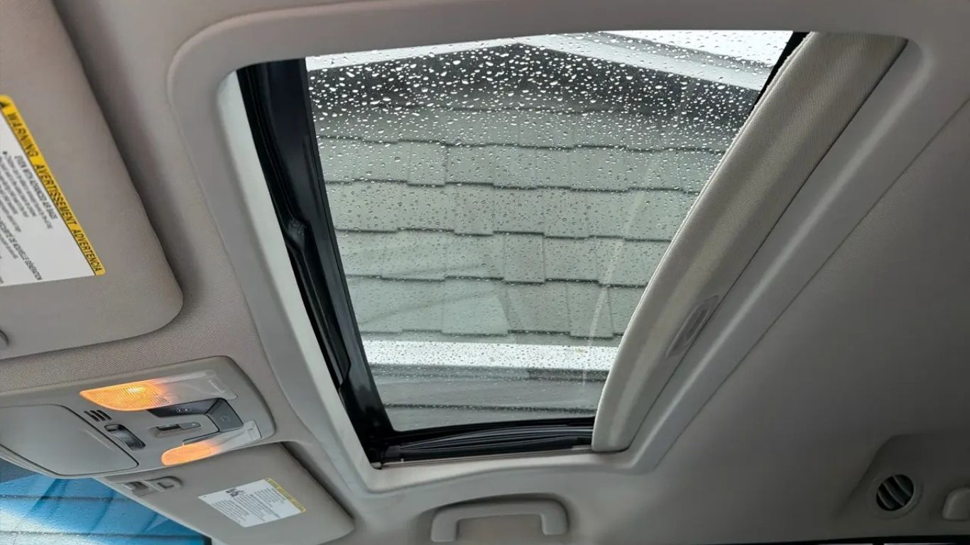 Car interior with a rain-speckled sunroof and overhead console lights on