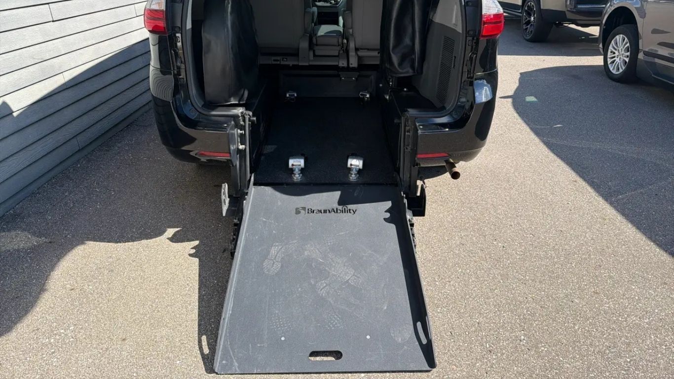 Rear view of a black van with its wheelchair ramp lowered into a parking lot.
